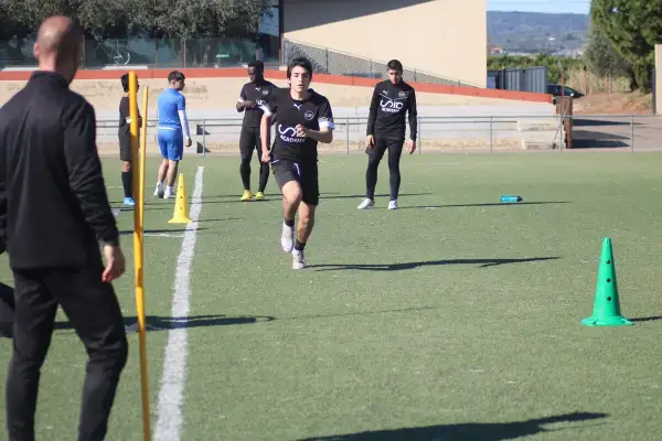 Jóvenes futbolistas realizan pruebas físicas en campo. Un entrenador de fútbol nivel 1 supervisa el entrenamiento.