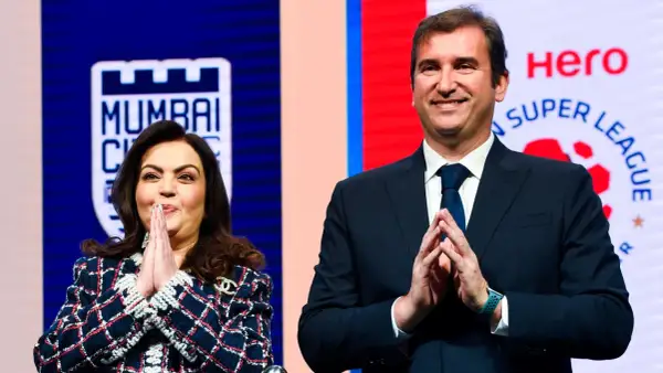 Nita Ambani y un hombre sonríen con las manos juntas, con el logo de la Superliga India de fondo.
