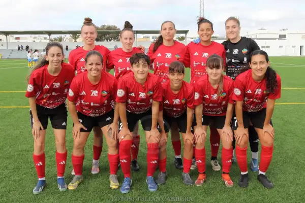 Equipo de fútbol femenino posando en el campo. Las jugadoras, con camisetas rojas y negras, muestran su espíritu deportivo.