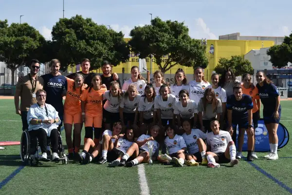 Equipo de fútbol femenino del Massanassa CF posa en el campo, con entrenadores y una persona en silla de ruedas.