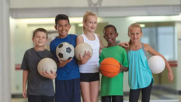 Cinco niños sonríen, cada uno con un balón. Uno sostiene un balón de baloncesto, listo para jugar.