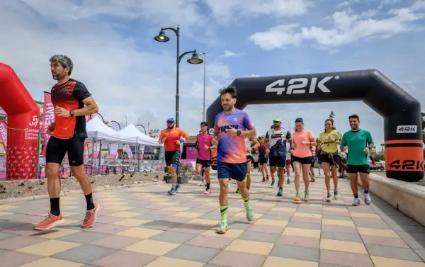 Corredores inician una carrera bajo un arco de 42K. La pregunta de cuanto dura un calentamiento se responde con la energía de estos atletas.