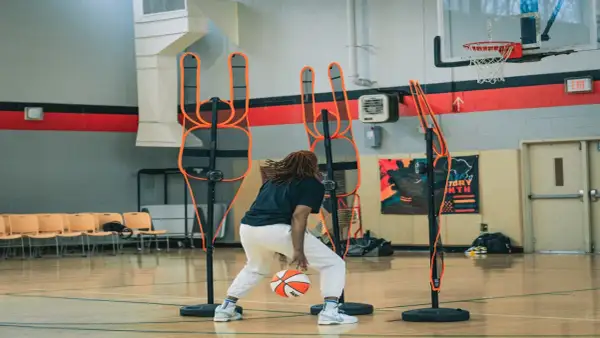 Jugador de baloncesto practica dribbling entre conos de entrenamiento en cancha interior.