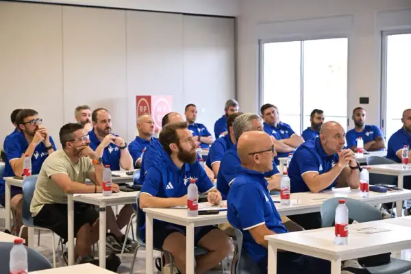 Un grupo de entrenadores España asiste a una charla en un aula, todos con polos azules.