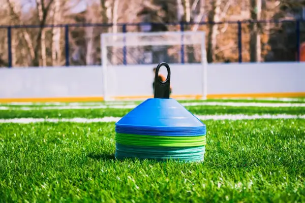 Conos de entrenamiento de fútbol apilados en césped verde, listos para una sesión. ¿Cuánto dura un entrenamiento de fútbol?