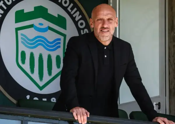 David Cabello, entrenador, posa con confianza frente al escudo de un club deportivo.