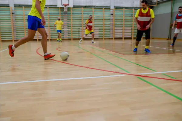 Jugadores realizan ejercicios individuales de fútbol sala en cancha de madera.