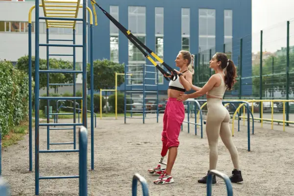 Dos mujeres entrenan en un gimnasio al aire libre. Una usa un sistema de entrenamiento en suspensión para un microciclo de impacto.