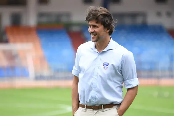 Carles Cuadrat sonríe en un campo de fútbol con gradas al fondo.