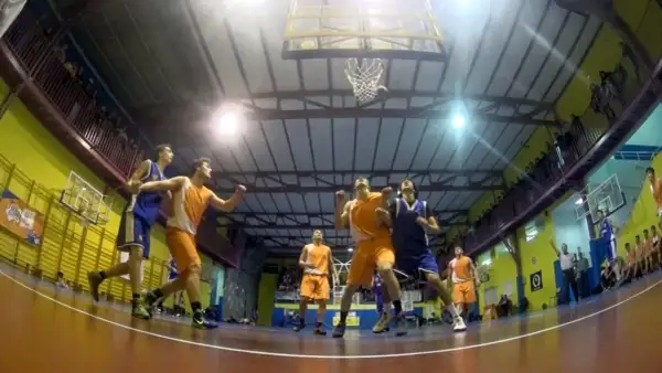 Jugadores de baloncesto compiten por un rebote bajo la canasta en un gimnasio.